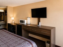 Una habitación de hotel con cama, escritorio con microondas, lámpara y televisor de pantalla plana.