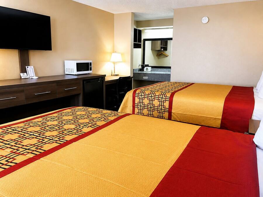 A hotel room with two beds, a desk, a television, a microwave, and a lamp.