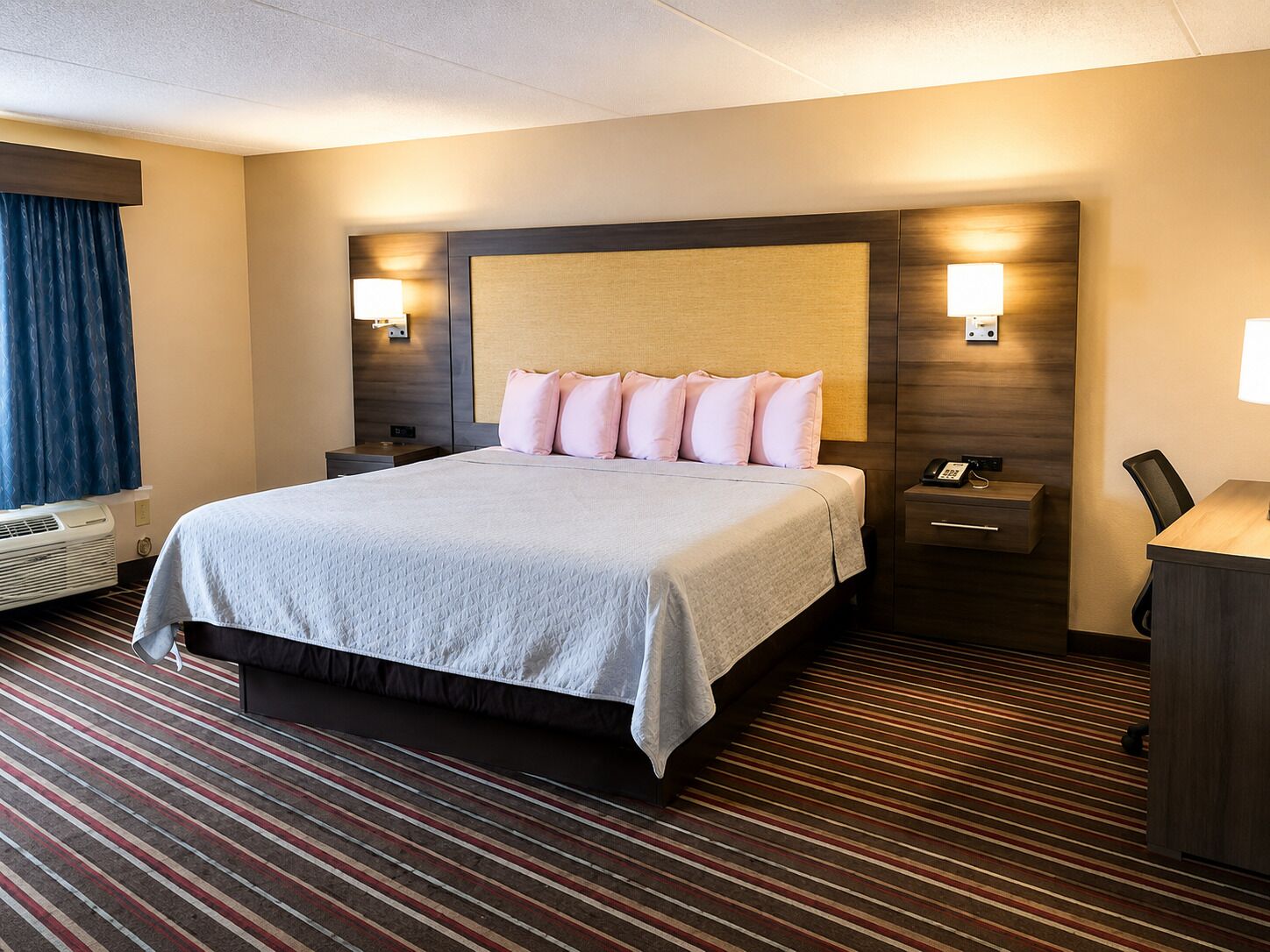 Ein Hotelzimmer mit einem großen Bett, Nachttischlampen, einem Schreibtisch mit Telefon und einem Vorhangfenster.