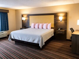 Una habitación de hotel con una cama grande, lámparas de noche, un escritorio con teléfono y una ventana con cortinas.