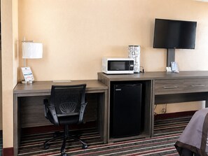 A hotel room with a desk, a microwave, a refrigerator, a TV, a chair, and a striped carpet. - Legacy Inn Sumner (Gallatin)