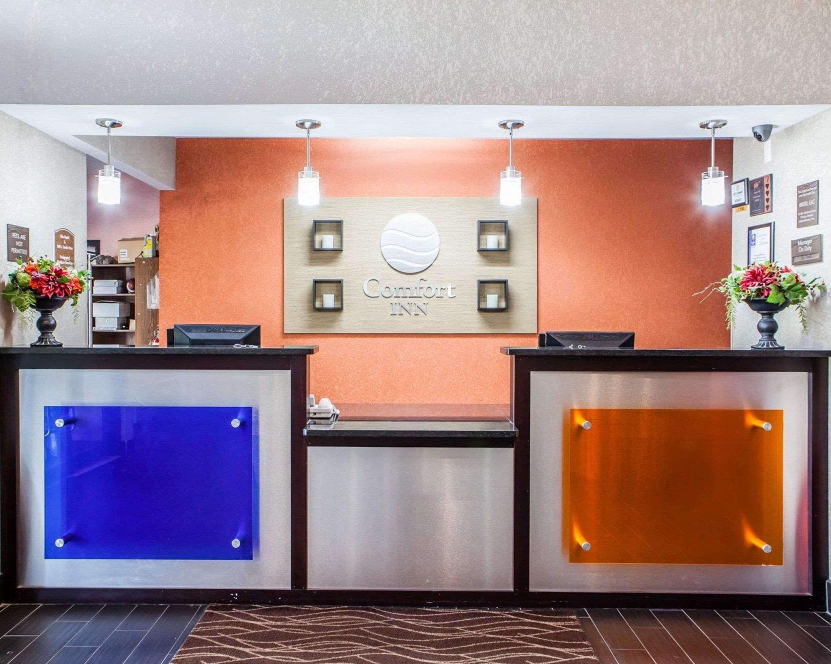 Een hotel receptiebalie met een bord waarop 'Comfort INN' staat, een modern ontwerp met twee glazen panelen en een houten accentmuur.