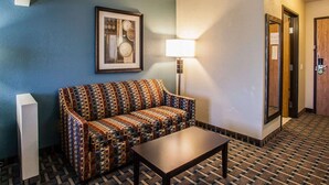 A hotel room with a patterned sofa, a table, a framed artwork on the wall, a lamp, and a carpeted floor. - Comfort Inn Lees Summit @ Hwy 50 & Hwy 291 (Lee's Summit)