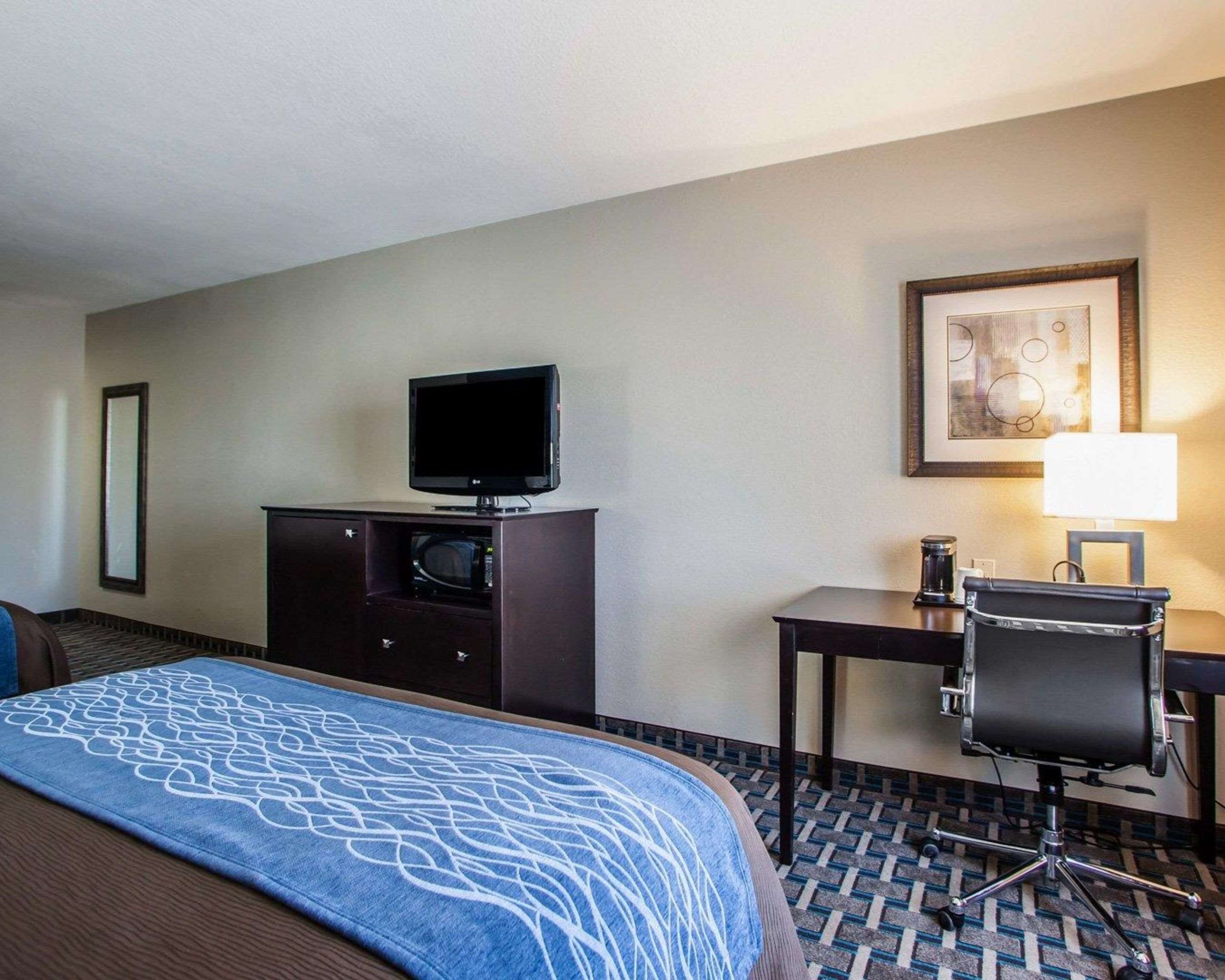 A hotel room with a bed, a TV on a dresser, a desk with a chair, and a framed picture on the wall.