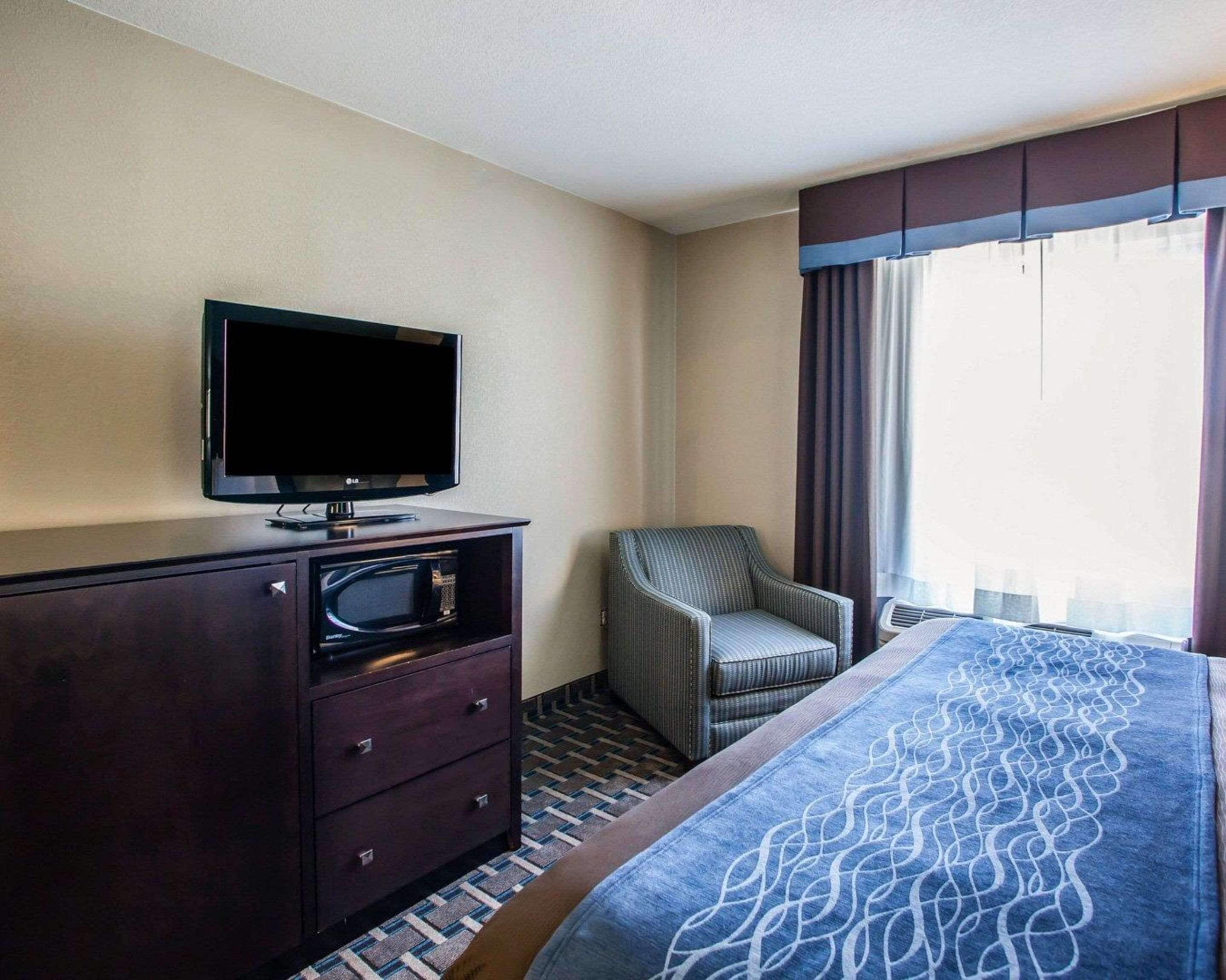 A hotel room with a bed, a television on a dresser, a chair, and a window with curtains.