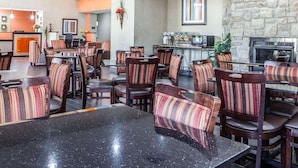 A hotel lobby with a stone wall, a fireplace, and a dining area with striped chairs and tables. - Comfort Inn Lees Summit @ Hwy 50 & Hwy 291 (Lee's Summit)