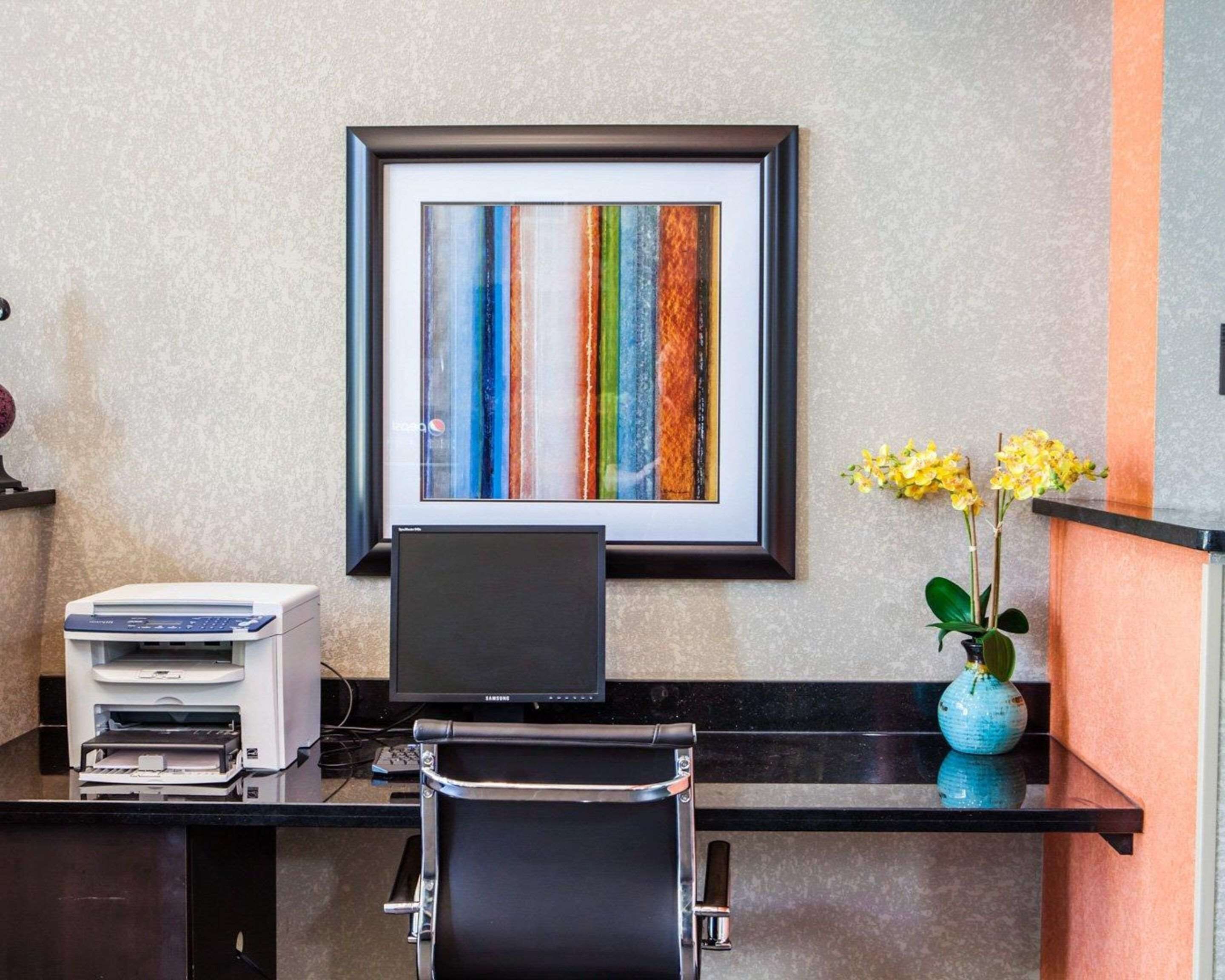 A modern office desk with a printer, a laptop, and a framed abstract painting on the wall.