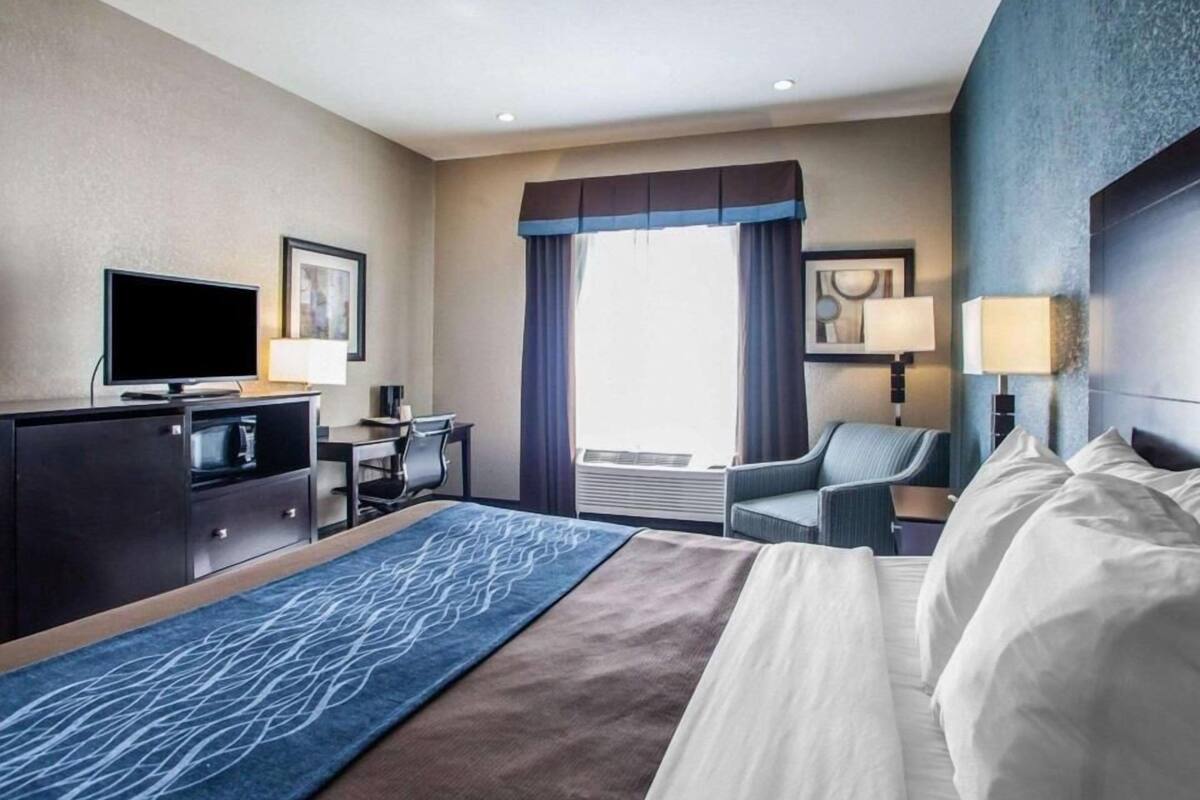 Habitación de hotel con cama, escritorio, televisor, silla y ventana con cortinas.