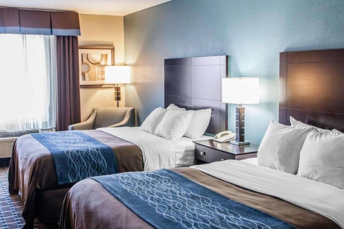 Habitación de hotel con dos camas, una mesita de noche, una lámpara, una silla y una ventana con cortinas.