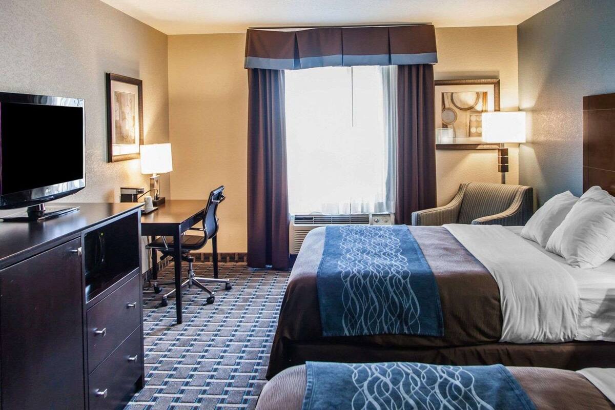 Habitación de hotel con cama, escritorio, silla, televisión y un ventanal con cortinas.