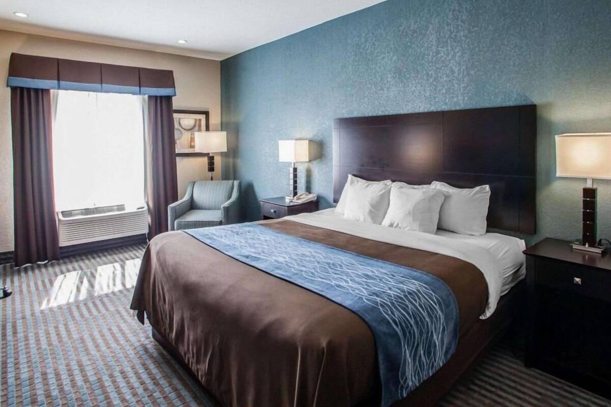 Habitación de hotel con una cama grande, dos mesitas de noche, una silla y una ventana con cortinas.