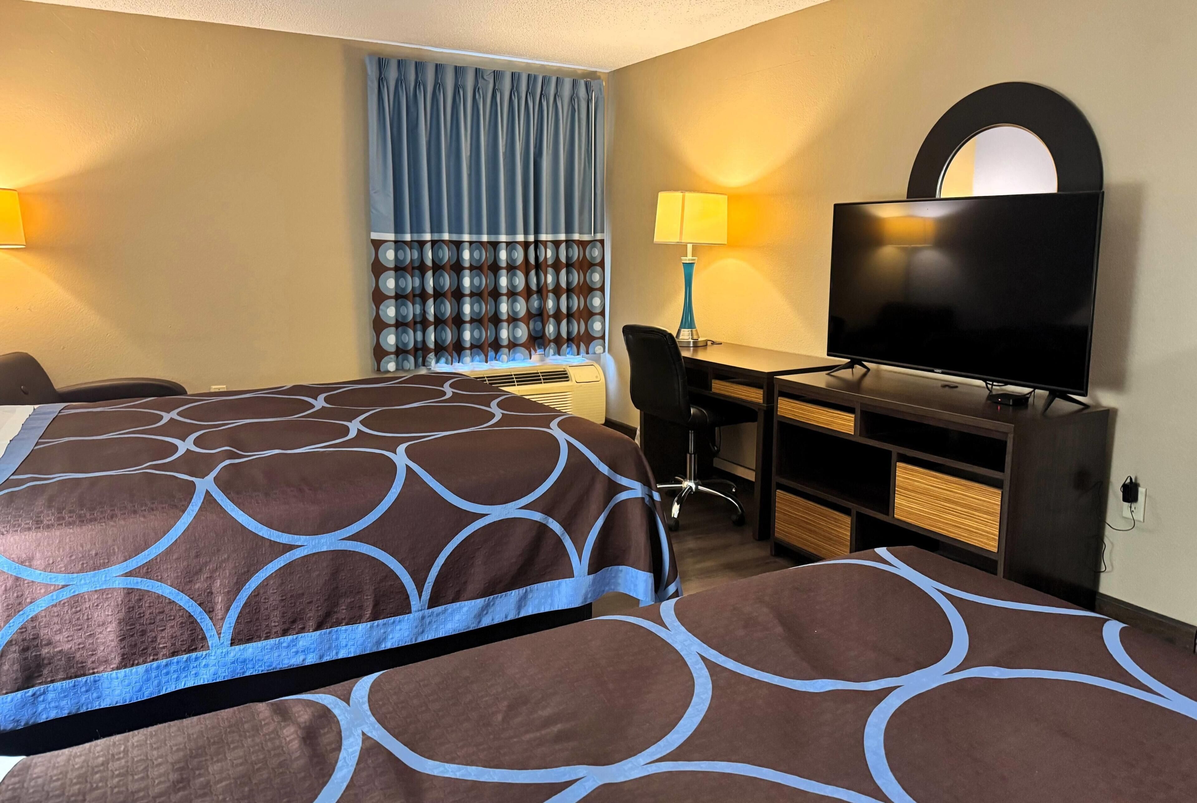 Een hotelkamer met twee bedden, een bureau met een televisie, een stoel en een lamp.