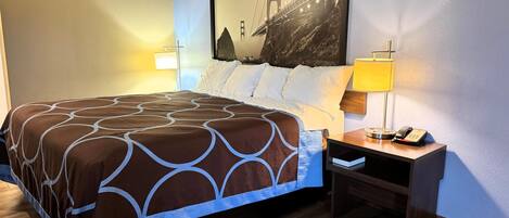 A hotel room with a bed, two bedside lamps, a nightstand with a phone, and a large wall painting of the Golden Gate Bridge.