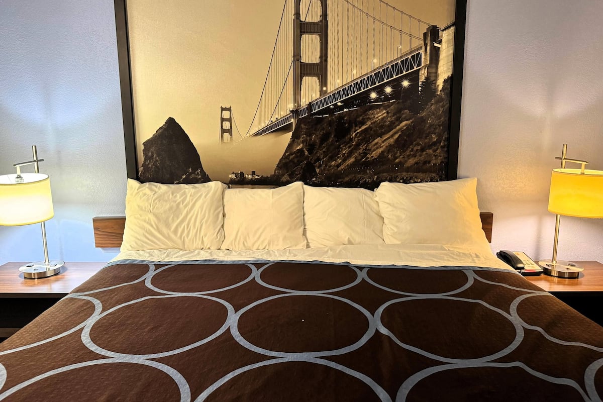 A hotel room with a bed, two bedside lamps, a phone, and a large wall mural of the Golden Gate Bridge.