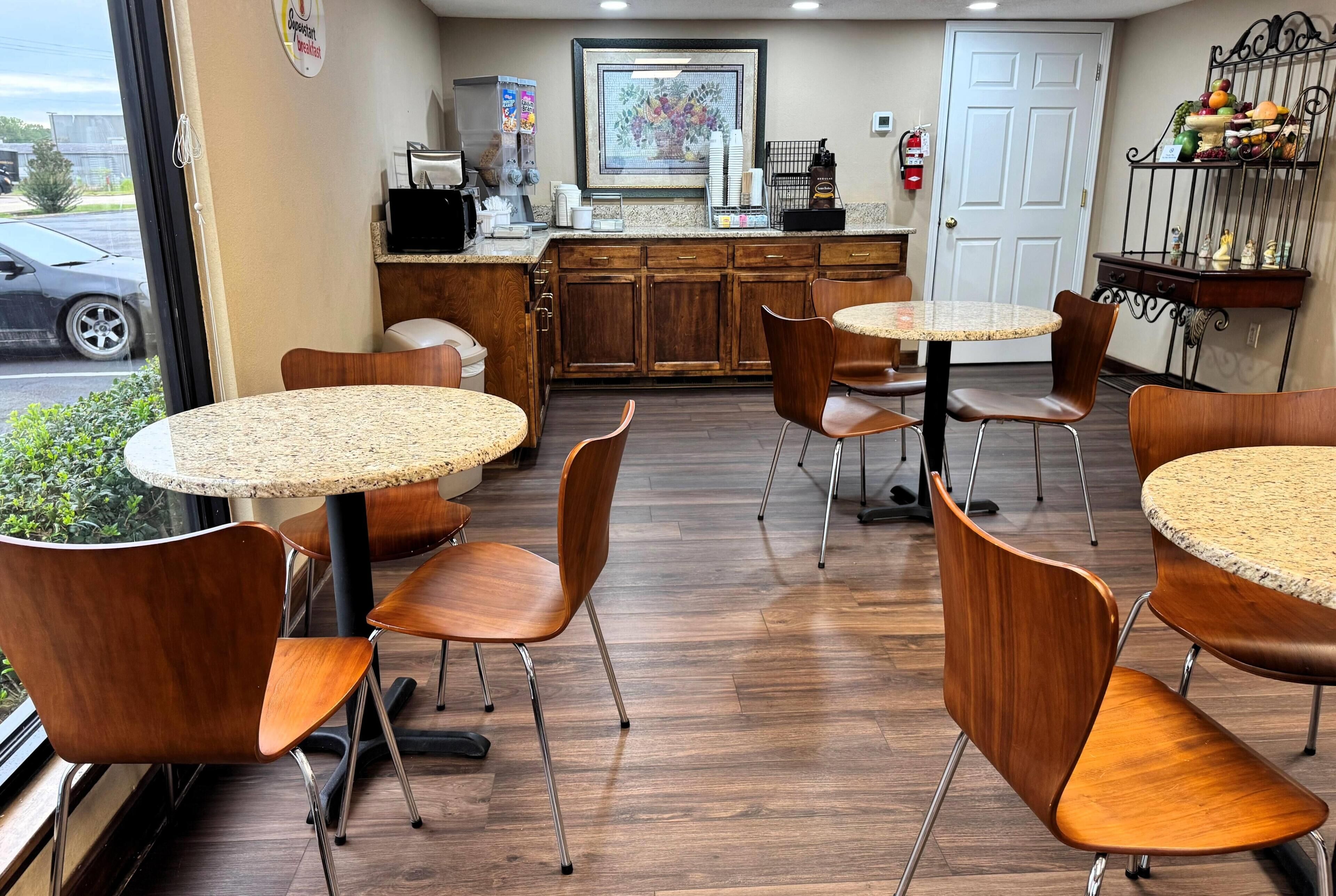 A restaurant with round tables and wooden chairs, a coffee machine, and a fruit display.
