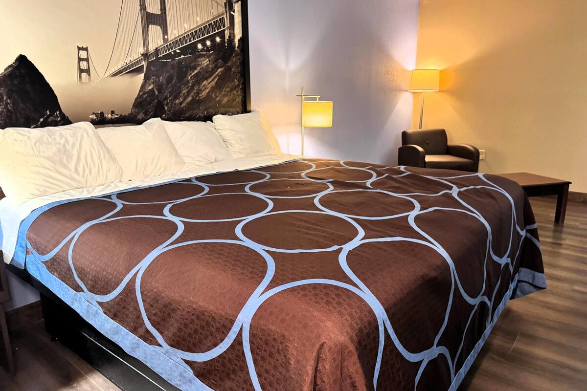 A hotel room with a large bed, a chair, a lamp, and a wall mural of a bridge.