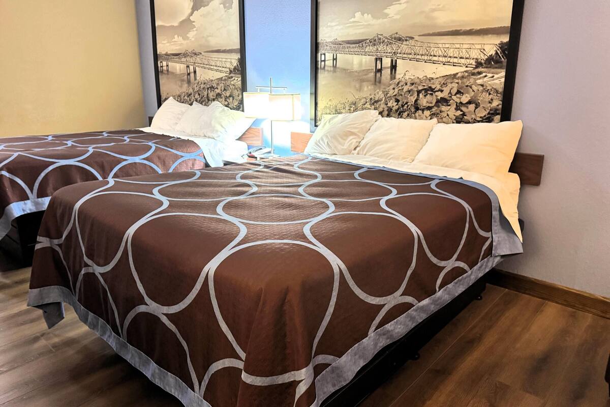 A hotel room with two beds, a large window with a view of a bridge, and a painting of a bridge on the wall.