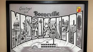 Una vista urbana en blanco y negro enmarcada, con el texto 'Greetings from Booneville' y 'Mississippi', un barco de vapor y un edificio con cúpula.
