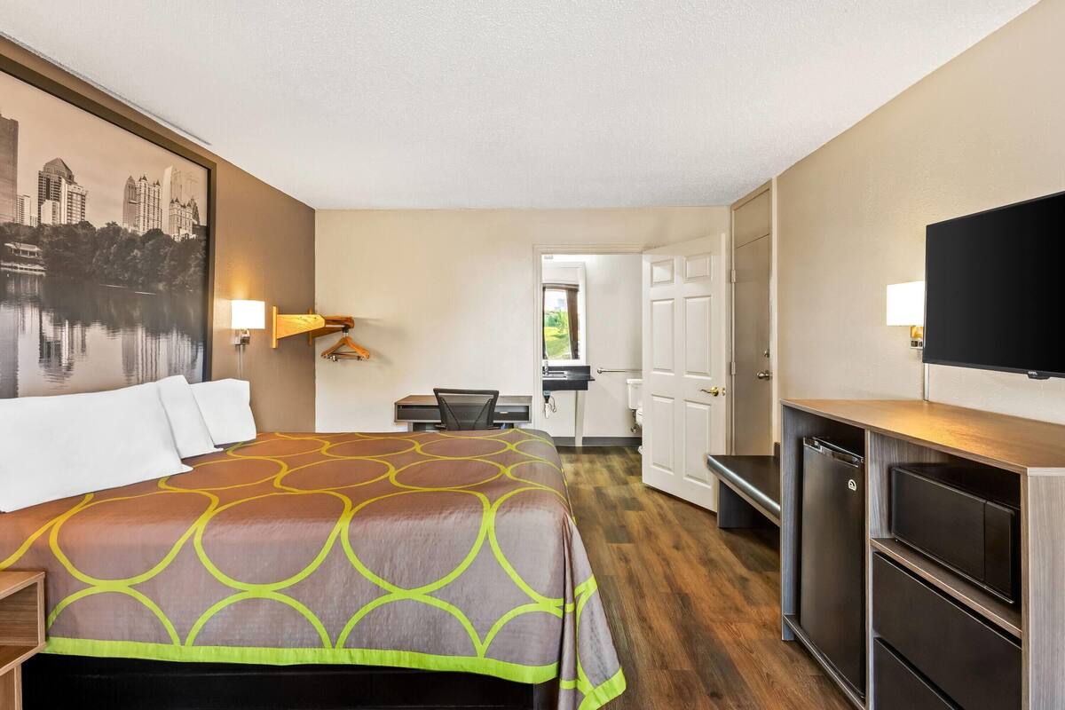 A hotel room with a large bed, a desk, a chair, a television, and a door leading to a bathroom.