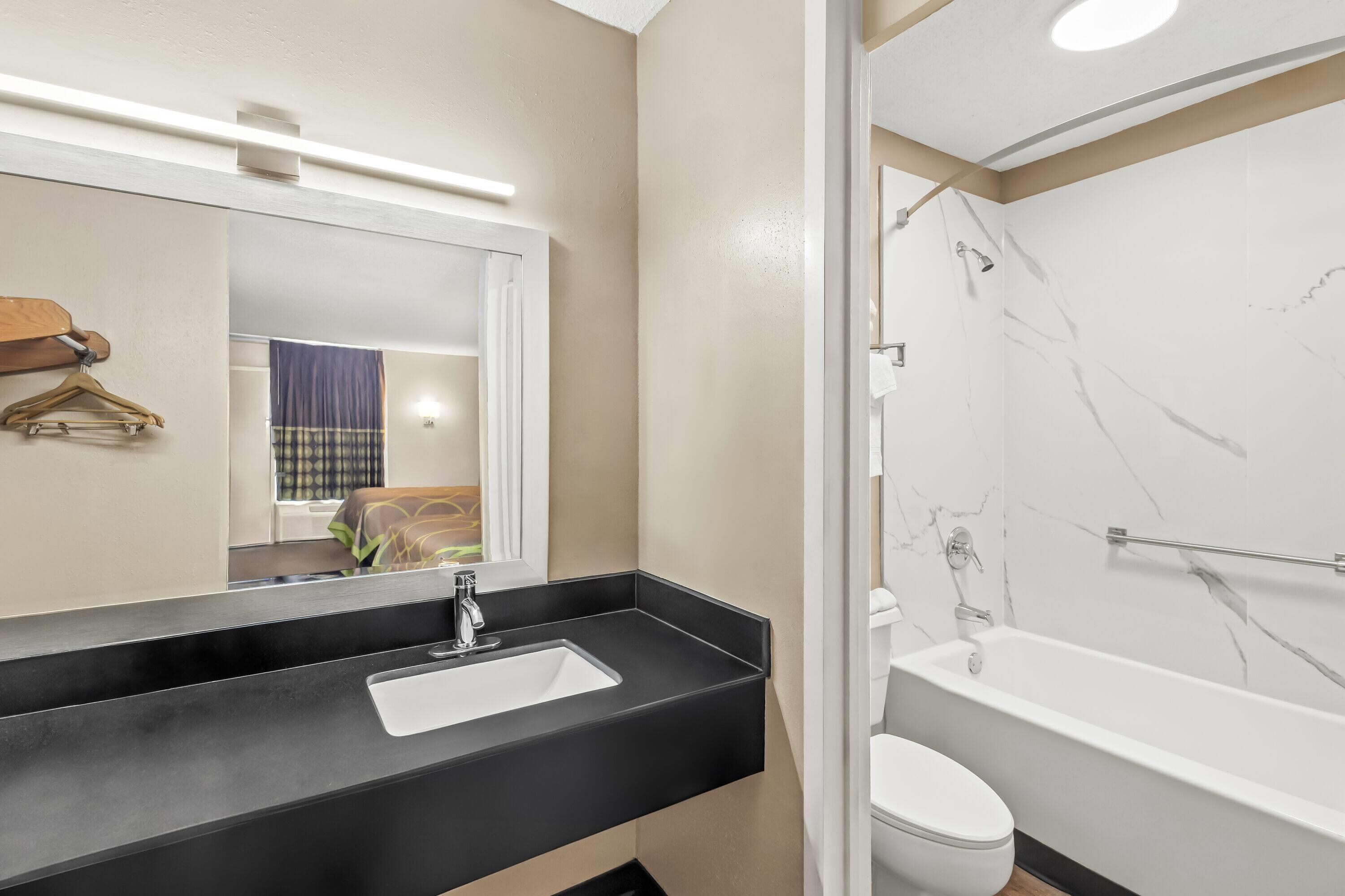A modern bathroom with a black countertop sink, a white toilet, and a bathtub with marble walls.