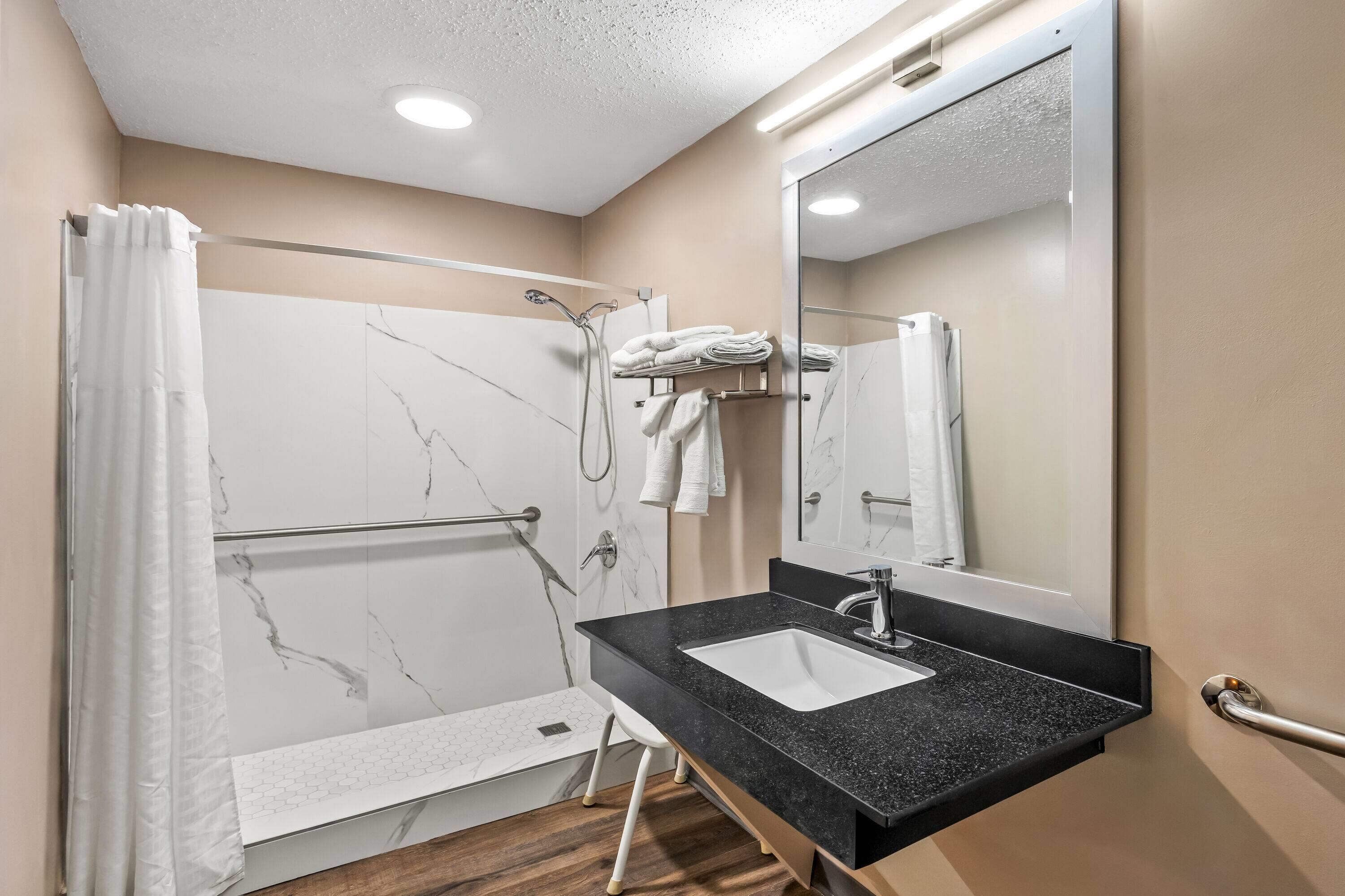 A modern bathroom with a marble shower, a black sink, and a large mirror.