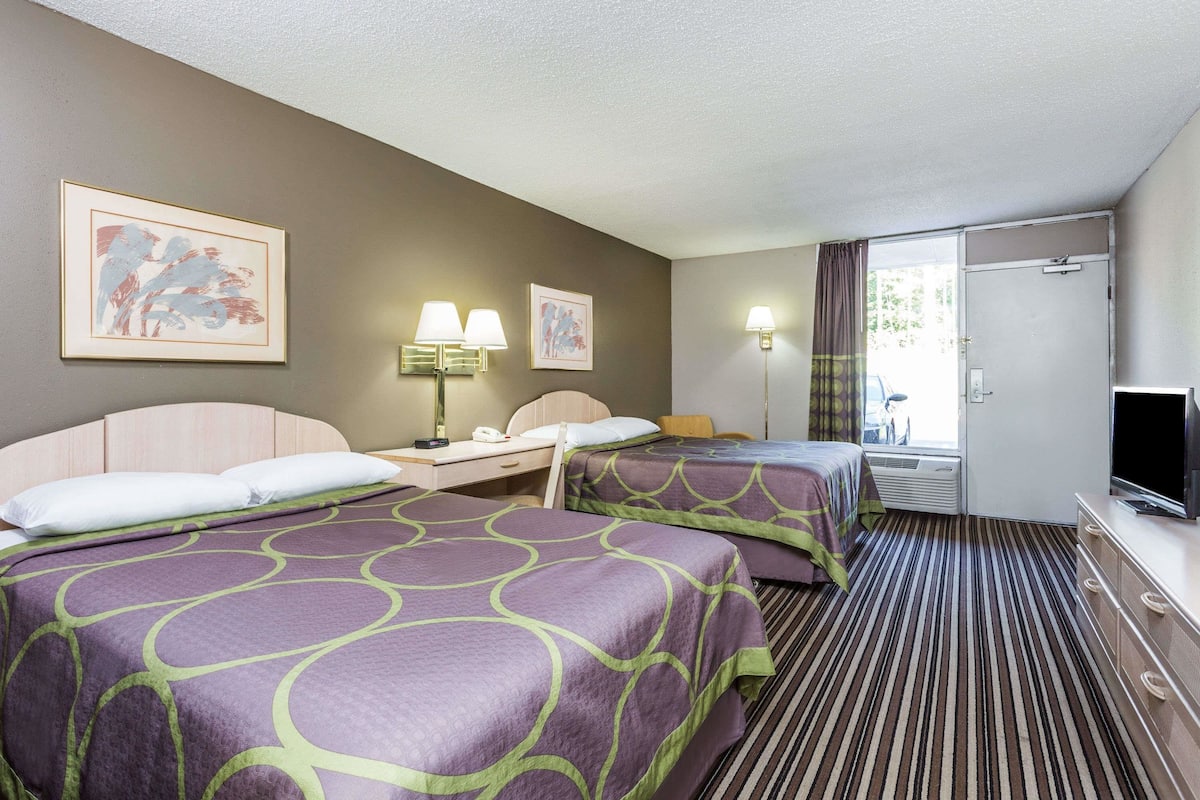 A hotel room with two beds, a desk, a television, and a window with curtains.