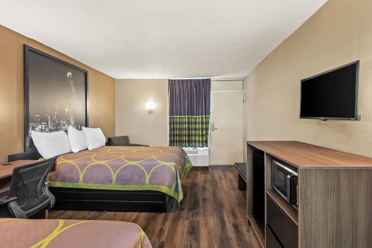 A hotel room with a bed, a desk, a chair, a TV, and a microwave.