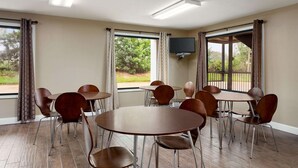 Une salle de conférence dotée de plusieurs tables et chaises, de grandes fenêtres avec des rideaux et d’un téléviseur à écran plat fixé au mur.