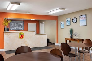 Ein Hotel-Empfangsbereich mit einer Rezeption, gerahmten Kunstwerken, einer Uhr und einem kleinen Tisch mit Stühlen.