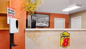Un comptoir d’accueil équipé d’un distributeur de gel hydroalcoolique, d’une pancarte d’accueil encadrée et du logo de « Super 8 ».