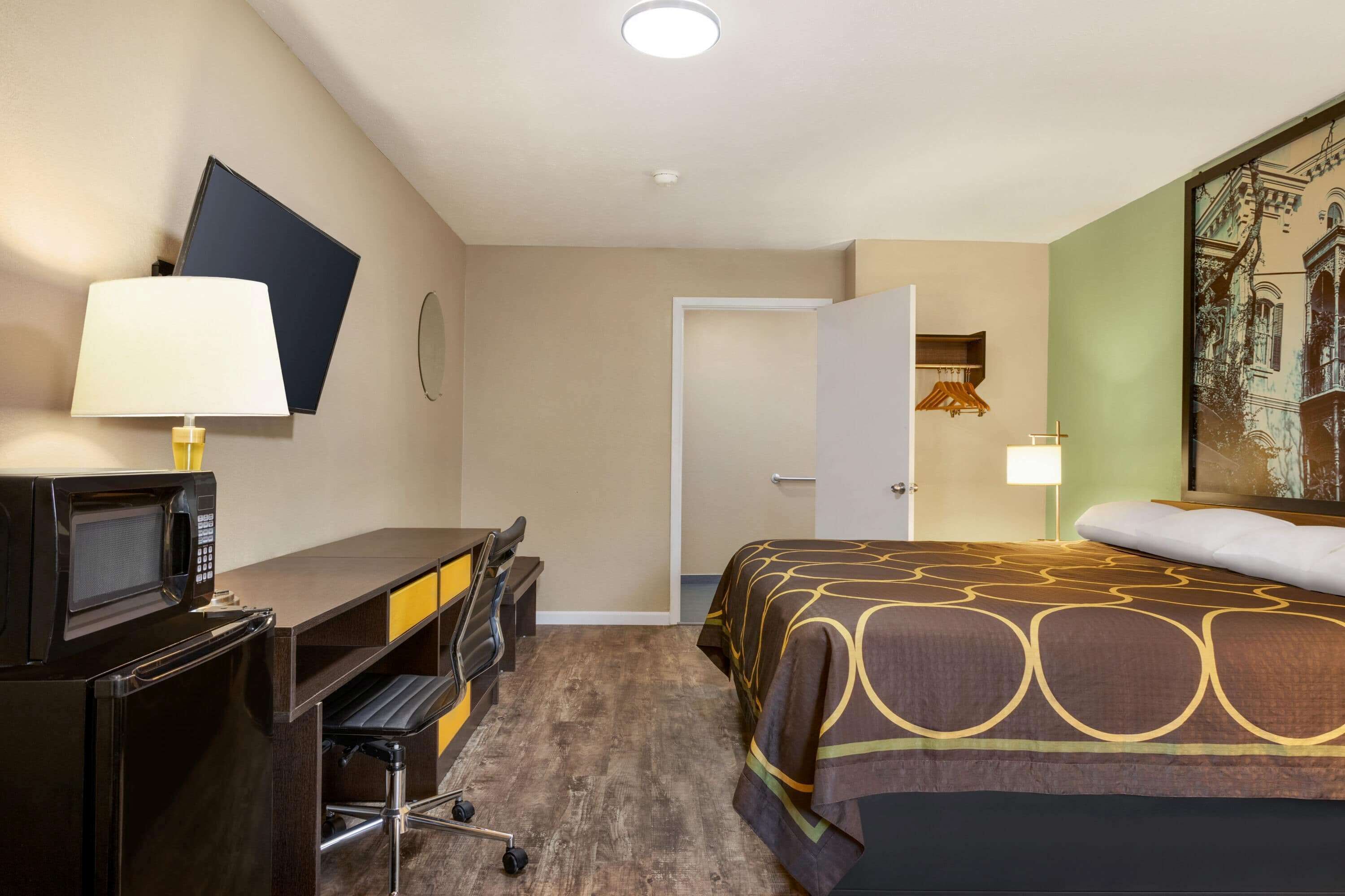 A hotel room with a bed, desk, chair, and a microwave.