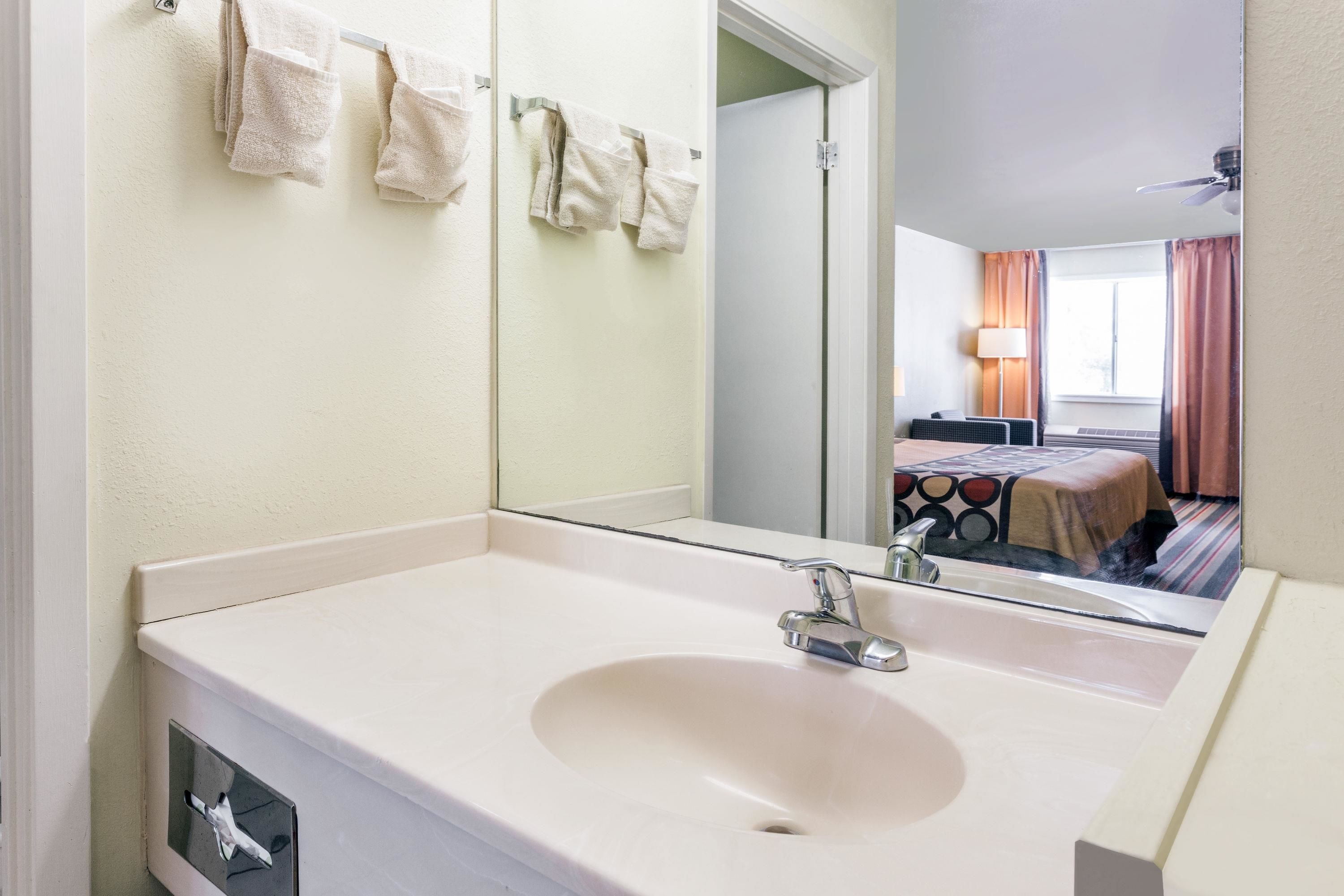 A hotel bathroom with a sink, mirror, and towels on a rack.