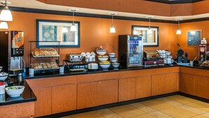 Een ontbijtruimte van een hotel met een lange balie, diverse etenswaren, een koffieapparaat en een koelkast.