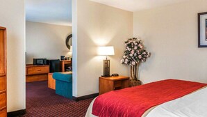 Een hotelkamer met een bed, een bureau met stoel, een lamp en een bloemenboeket.