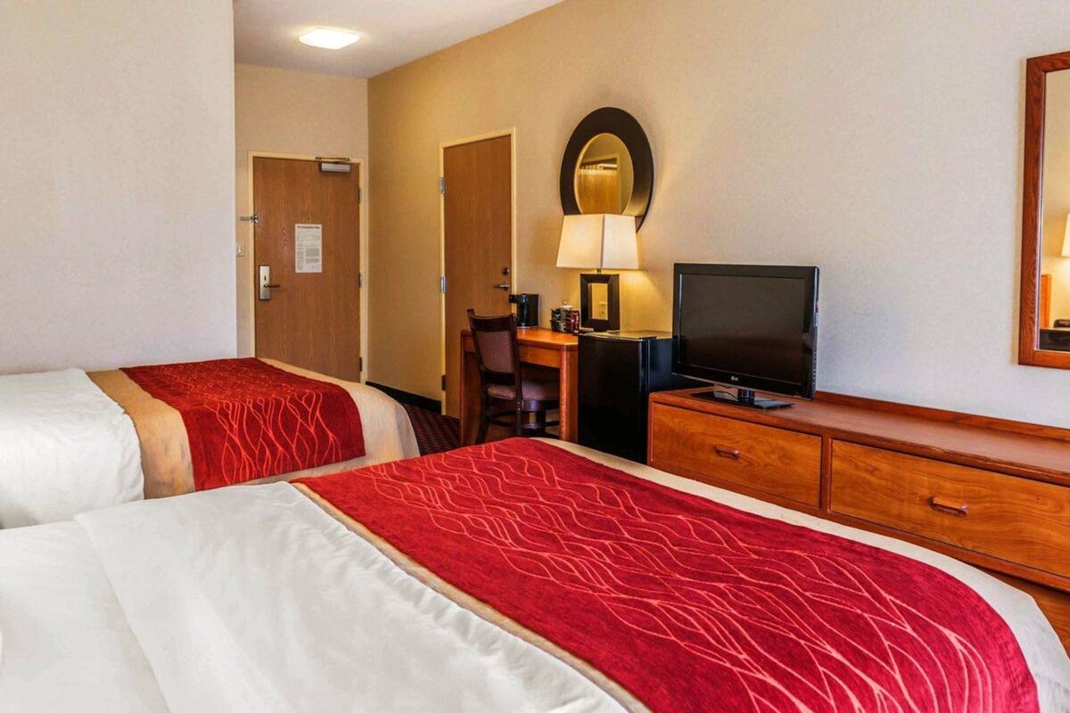 A hotel room with two beds, a desk with a television, a mirror, and a lamp.