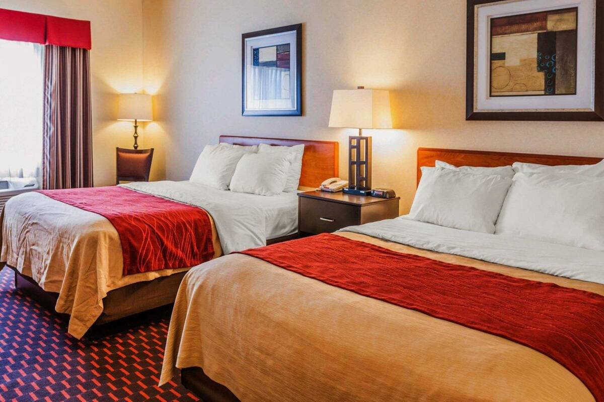 A hotel room with two beds, a nightstand with a lamp, a framed picture on the wall, and a window with curtains.
