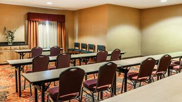 A conference room with long tables and chairs, a window with curtains, and a carpeted floor.