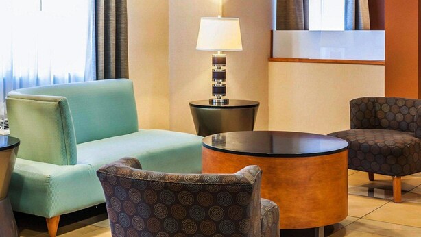 Een hotel lobby met een groene bank, gestreept fauteuils, een ronde tafel en een lamp.