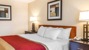 Un cuarto de hotel con una cama grande, un cabecero de madera, dos mesitas de noche con lámparas y cuadros en las paredes.