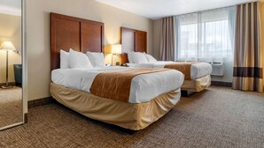 A hotel room with two beds, a large mirror, a window with curtains, and a wall-mounted air conditioner.