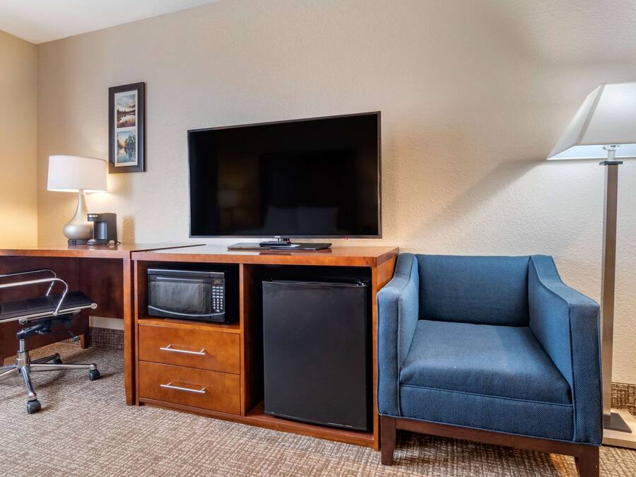 Une chambre d’hôtel avec un bureau en bois, un téléviseur à écran plat, un four à micro-ondes, un mini-réfrigérateur, un canapé bleu, une lampe de bureau et un tableau encadré au mur.