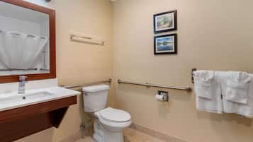 Ein Badezimmer mit Waschbecken, Toilette und Haltegriffen. An der Wand befinden sich zwei gerahmte Bilder und Handtücher auf einem Ablagegestell.