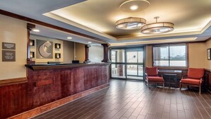A hotel lobby with a reception desk, a clock, and a seating area with two chairs.