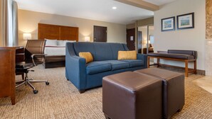 A hotel room with a blue sofa, a brown ottoman, a desk, and a chair.