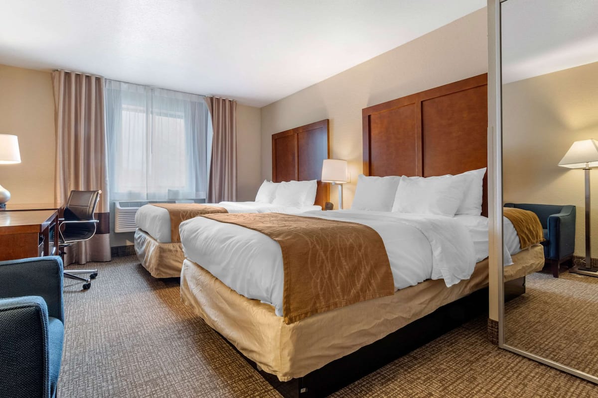 A hotel room with two beds, a desk, a chair, and a large mirror.