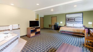 A hotel room with a large bed, a TV, a desk, and a bathroom with a bathtub.