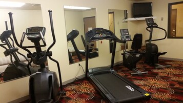 Gimnasio de hotel con varias máquinas de ejercicio, incluyendo cintas de correr y elípticas, y un espejo grande.