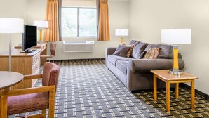 A hotel room with a sofa, a desk with a TV, a chair, a small table, and a patterned carpet.