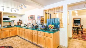 A kitchen with wooden cabinets, a green countertop, and a microwave. There is a dining area with a TV and a patterned rug.