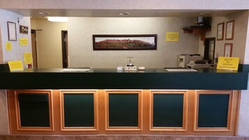 Un mostrador de recepción con un cuadro enmarcado encima, un cartel que indica la hora de registro y un aviso sobre el sistema de rociadores del edificio.